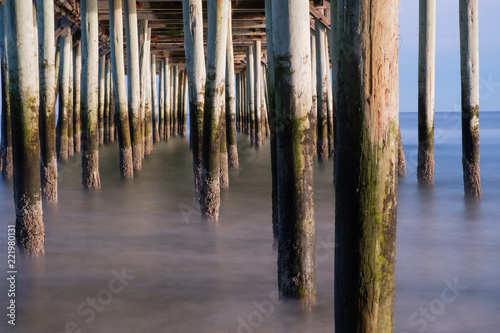 Moss covered wood pilings under the Old Orchard Beach Pier in Maine at low tide with small waves washing up