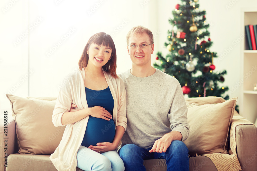 pregnancy, winter holidays and people concept - happy pregnant wife with husband at home at christmas