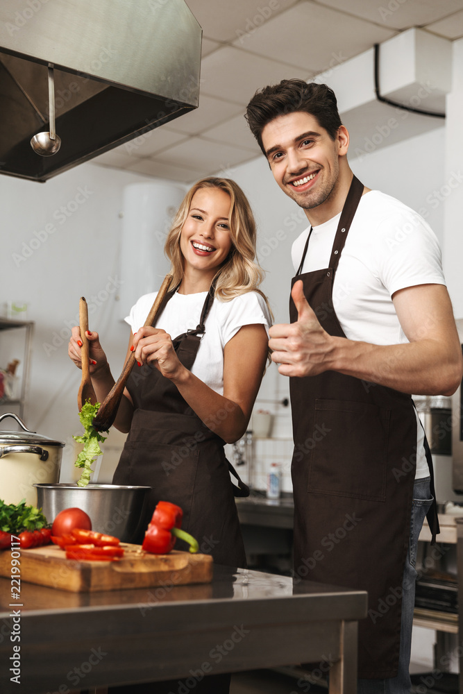 Smiling excited young friends loving couple chefs on the kitchen cooking. Smiling excited young friends loving couple chefs on the kitchen cooking.