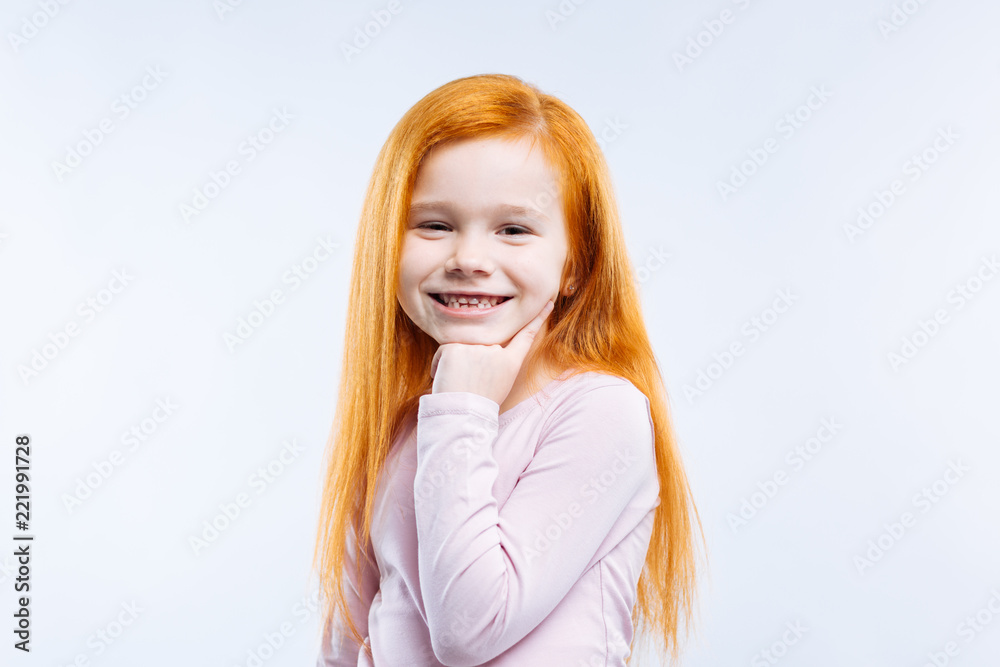 Friendly child. Joyful positive girl holding her chin while friendly smiling to you Friendly child. Joyful positive girl holding her chin while friendly smiling to you