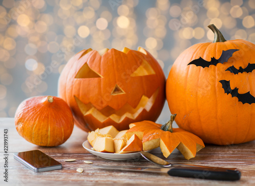 holidays, halloween and technology concept - jack-o-lantern or carved pumpkin with smartphone and knife on wooden table at home photo