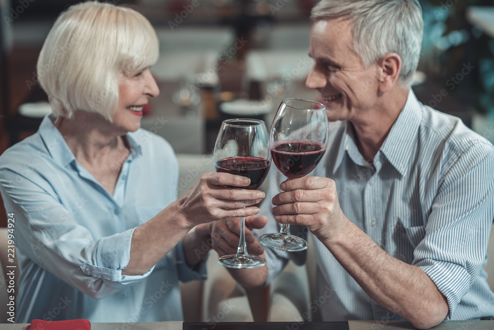 Pleasant relations. Delighted mature woman keeping smile on her face while going to drink wine Pleasant relations. Delighted mature woman keeping smile on her face while going to drink wine