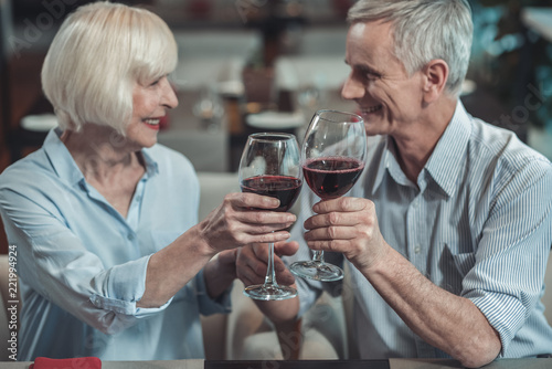 Pleasant relations. Delighted mature woman keeping smile on her face while going to drink wine