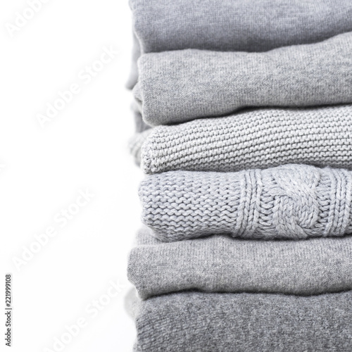 Careful stack of grey woolen and cashmere sweaters on white background