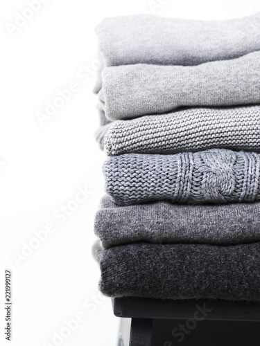 Careful stack of grey woolen and cashmere sweaters on white background