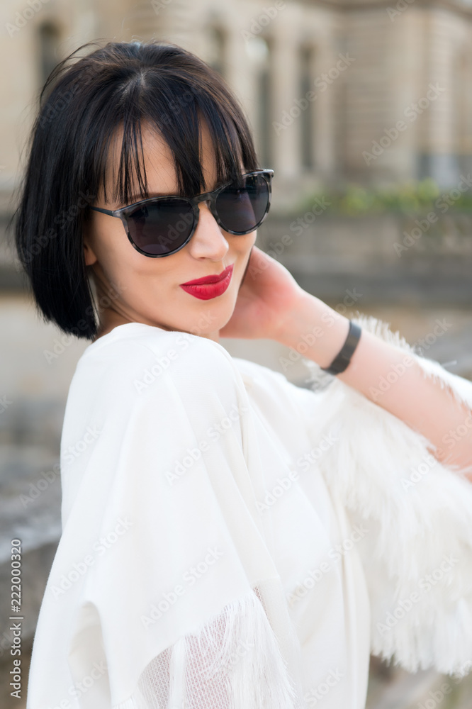 Hide her emotion behind sunglasses. Girl brunette bob hairstyle looks stylish. Girl fashionable lady with bob hairstyle outdoor urban architecture background. Woman fashionable model posing outdoor