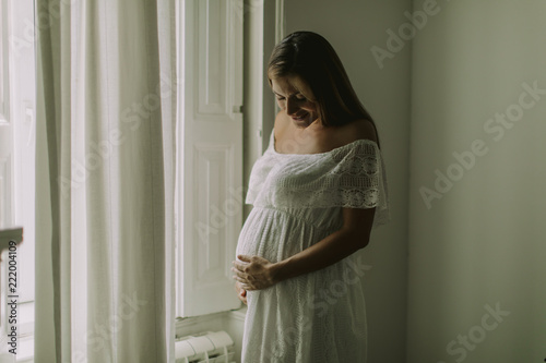 Young pregnant woman standing by the window