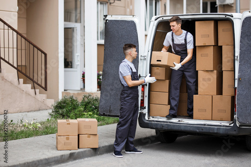 Two young handsome movers wearing uniforms are unloading the van