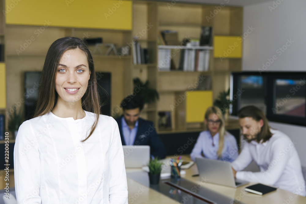 Young businesswoman standing in the office and other young business people working in the background