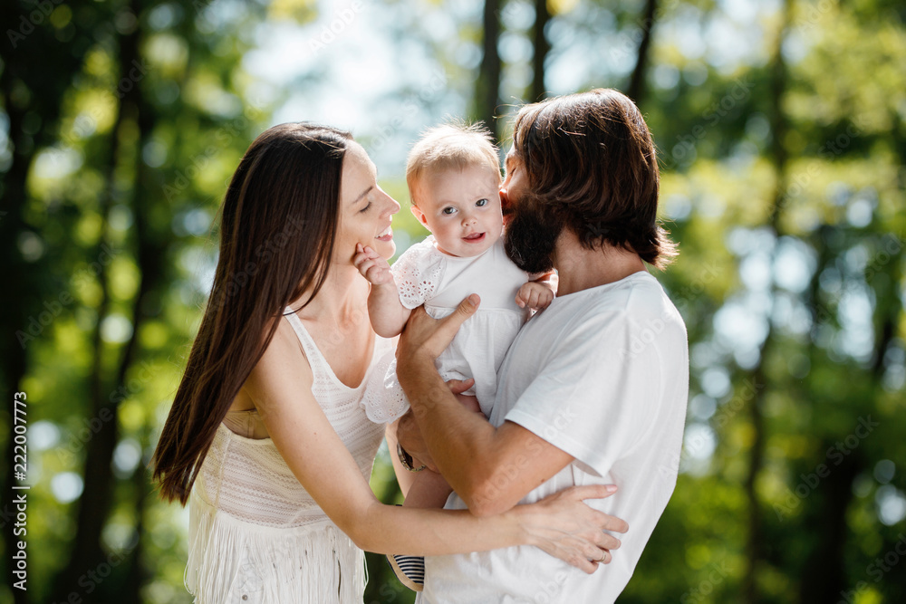 Happy beautiful parents dressed in the white casual clothes spending sunny day in the park with there little daughter. Happy beautiful parents dressed in the white casual clothes spending sunny day in the park with there little daughter.