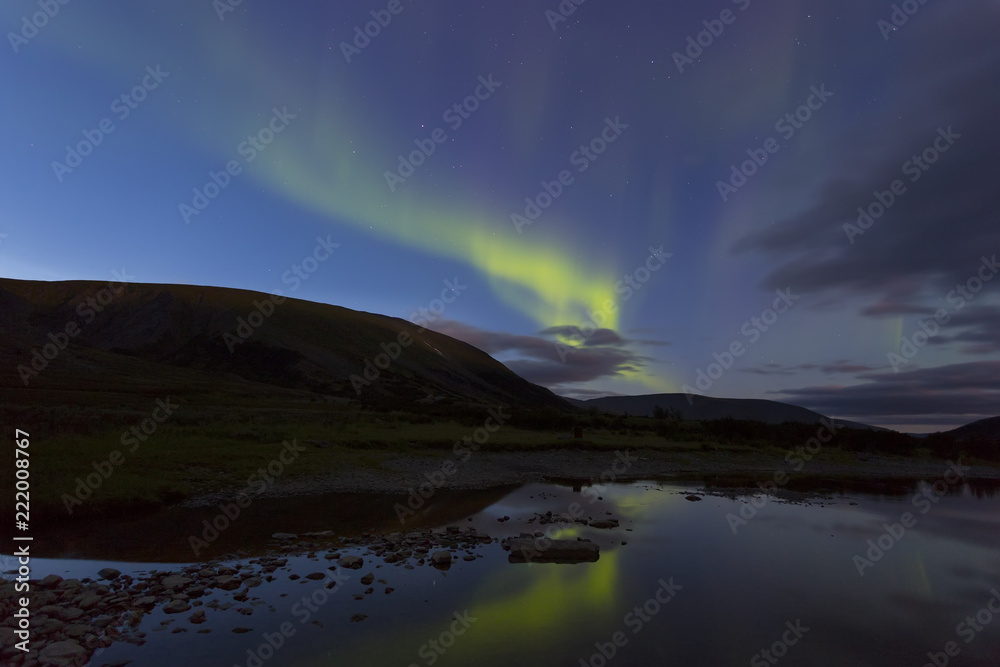 Aurora in the night sky cut the mountains, reflected in the water. Yamal. Russia