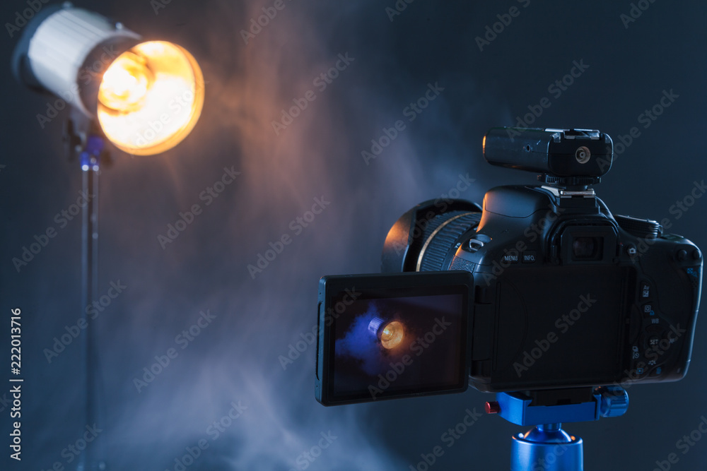 Photo of the camera on a blue tripod that photographs in the studio a professional lighting device in the smoke. Studio lights and smoke equipment. Advertising photo session of the lighting device Photo of the camera on a blue tripod that photographs in the studio a professional lighting device in the smoke. Studio lights and smoke equipment. Advertising photo session of the lighting device