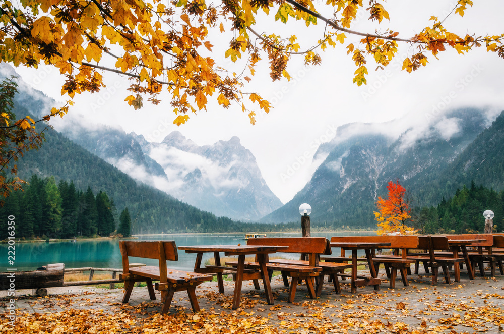 Naklejka premium Dobbiaco Lake or Toblacher in Dolomites with wooden tables and benches in outdoor cafe restaurant in autumn