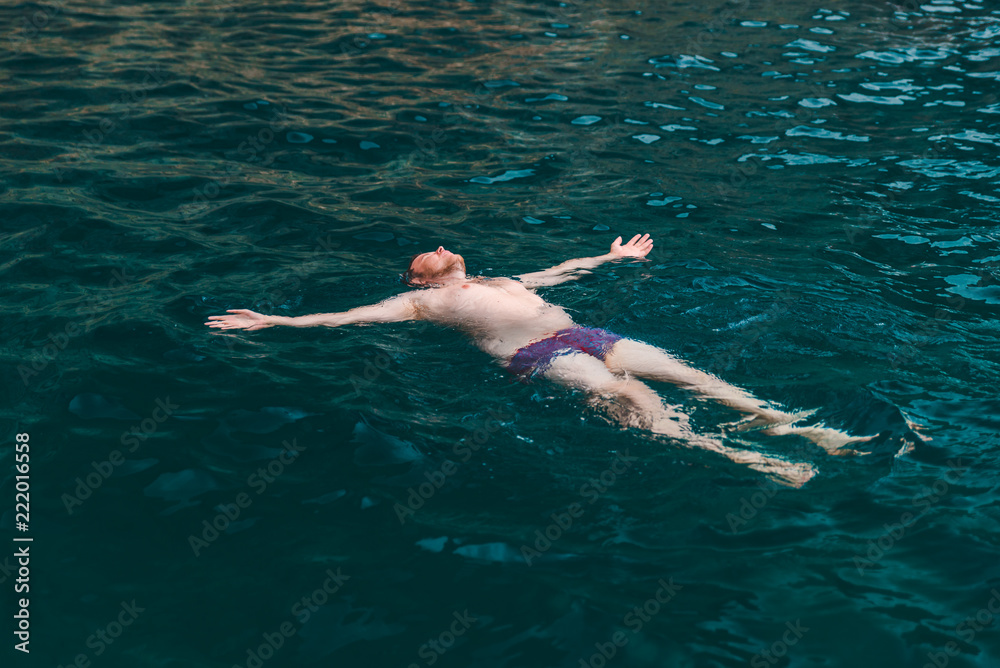 man swimming on back in blue transparent sea water