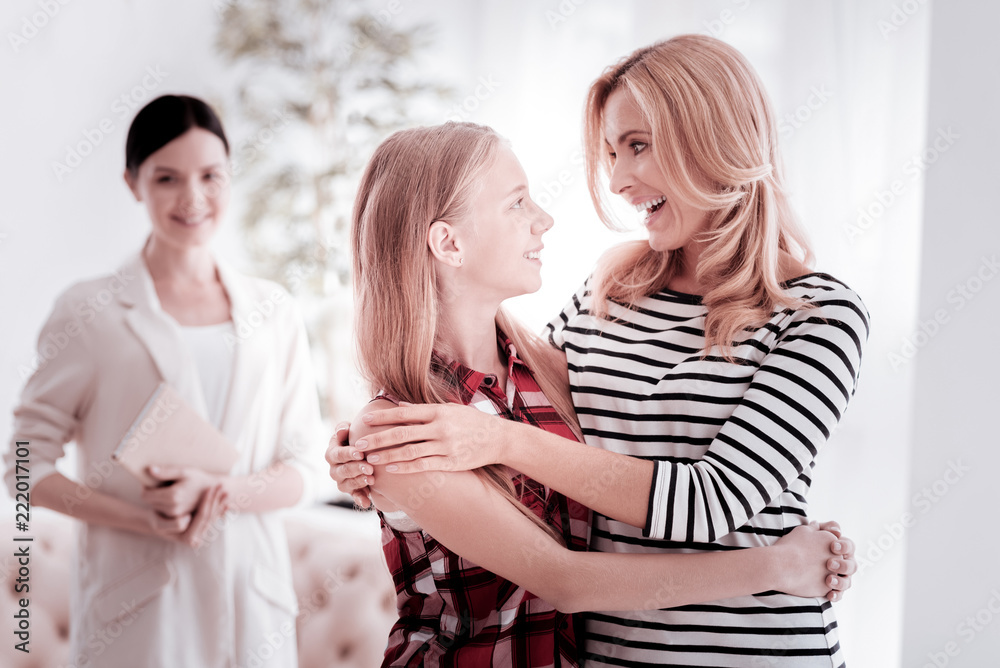 Happiness. Cheerful emotional young woman smiling and feeling happy while standing with her daughter and hugging her Happiness. Cheerful emotional young woman smiling and feeling happy while standing with her daughter and hugging her