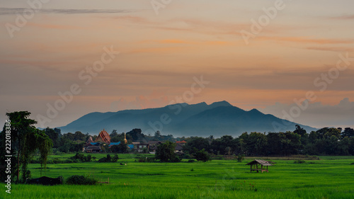 View of rural village in the evening..The temple, the field, the mountain.Thailand.