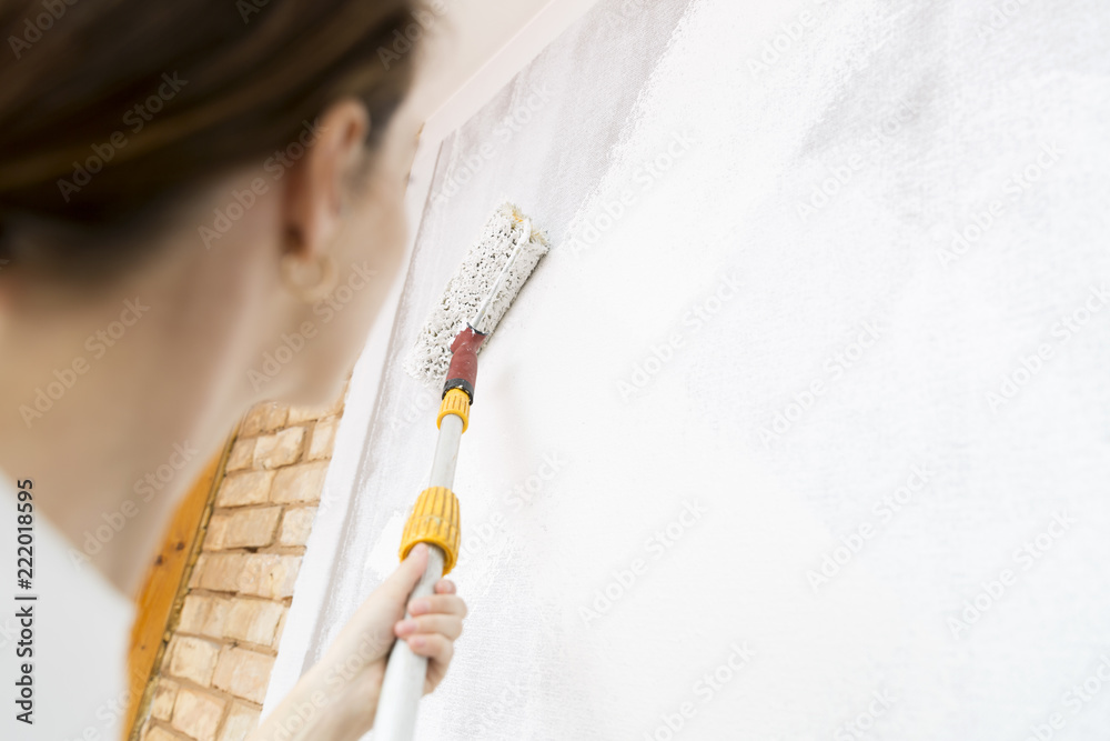 Home improvement. Beautiful woman painting wall with paint roller.