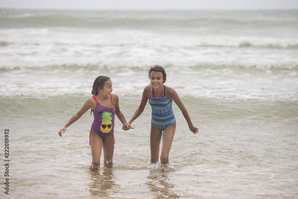 Two mixed-race sisters playing and laughing having fun on the beach on a bright tropical summer holiday