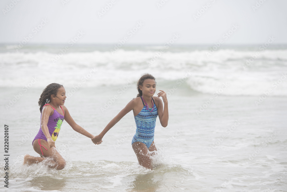 Two mixed-race sisters playing and laughing having fun on the beach on a bright tropical summer holiday