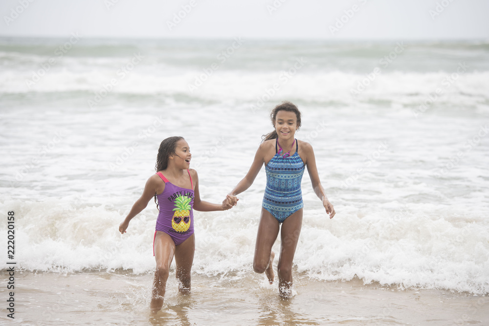 Two mixed-race sisters playing and laughing having fun on the beach on a bright tropical summer holiday