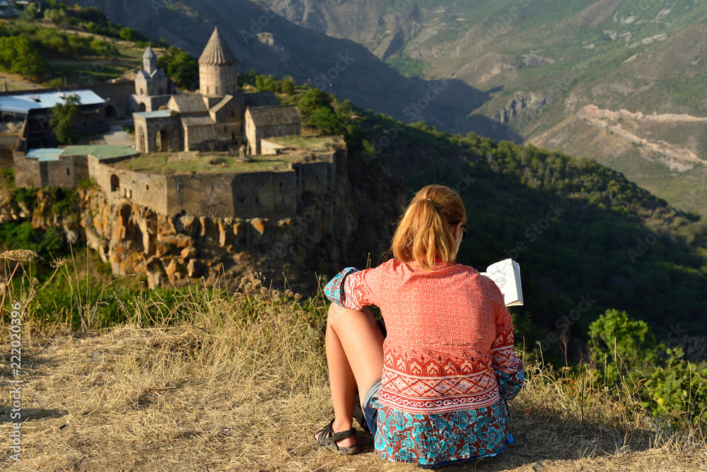 Φωτογραφία The tourist with the book is sitting on the grass in the background of the mount