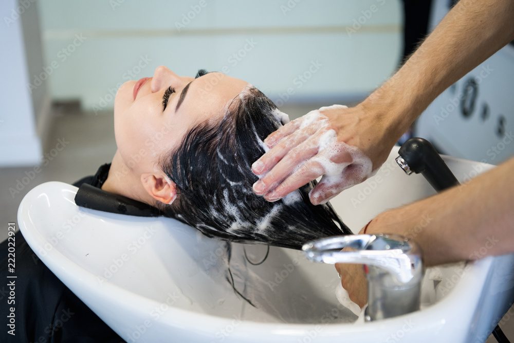 Unrecognizable professional hairdresser washing hair to her client. Beautiful hairdresser washing hair to her client lady in hairdressing saloon. Client sitting with her eyes closed. Unrecognizable professional hairdresser washing hair to her client. Beautiful hairdresser washing hair to her client lady in hairdressing saloon. Client sitting with her eyes closed.