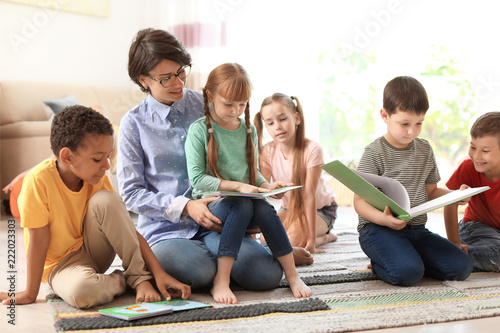 Young woman reading book to little children indoors. Learning by playing