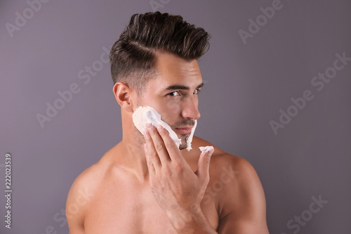 Handsome young man applying shaving foam on color background photo