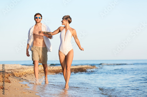 Happy young couple walking together on beach. Space for text