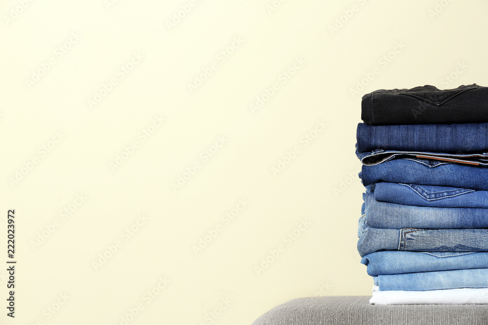 Stack of different jeans on ottoman against light background. Space for text Stack of different jeans on ottoman against light background. Space for text