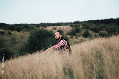 handsome male hipster sits in a field on the ground with tall grass