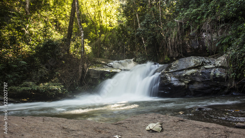 Long exposure of adorable, small waterfall surrounded by lush green foliage in Mae Klang Luang. Chiang Mai, Thailand.