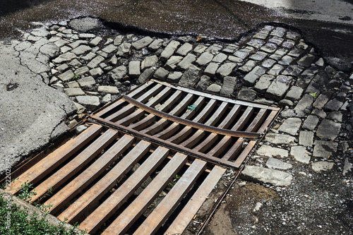 drainage sewer grate on the old road from the broken asphalt and paving blocks wet after the rain in one of the central streets of the city's greater