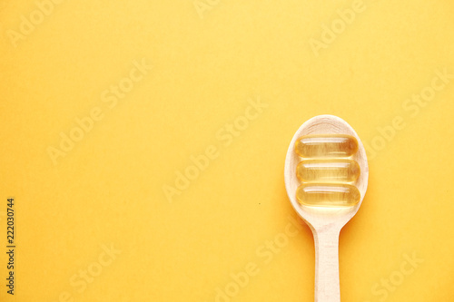 Three omega 3 fish liver oil capsules in wooden spoon. Big golden translucent pills on yellow background. Healthy every day fatty acids nutritional supplement. Top view, flat lay, copy space, close up