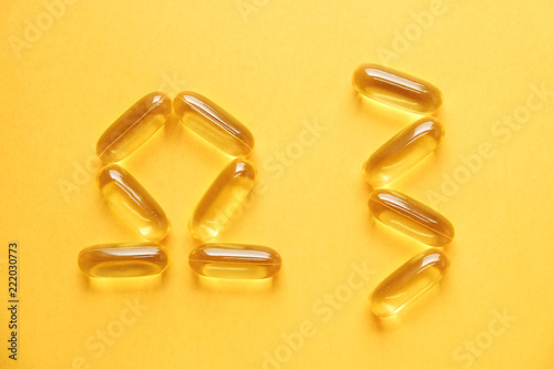Omega 3 symbol laid with fish liver oil capsules. Close up of big golden translucent in form of greek letter and digit. Healthy fatty acids nutritional supplement. Top view, flat lay, copy space.