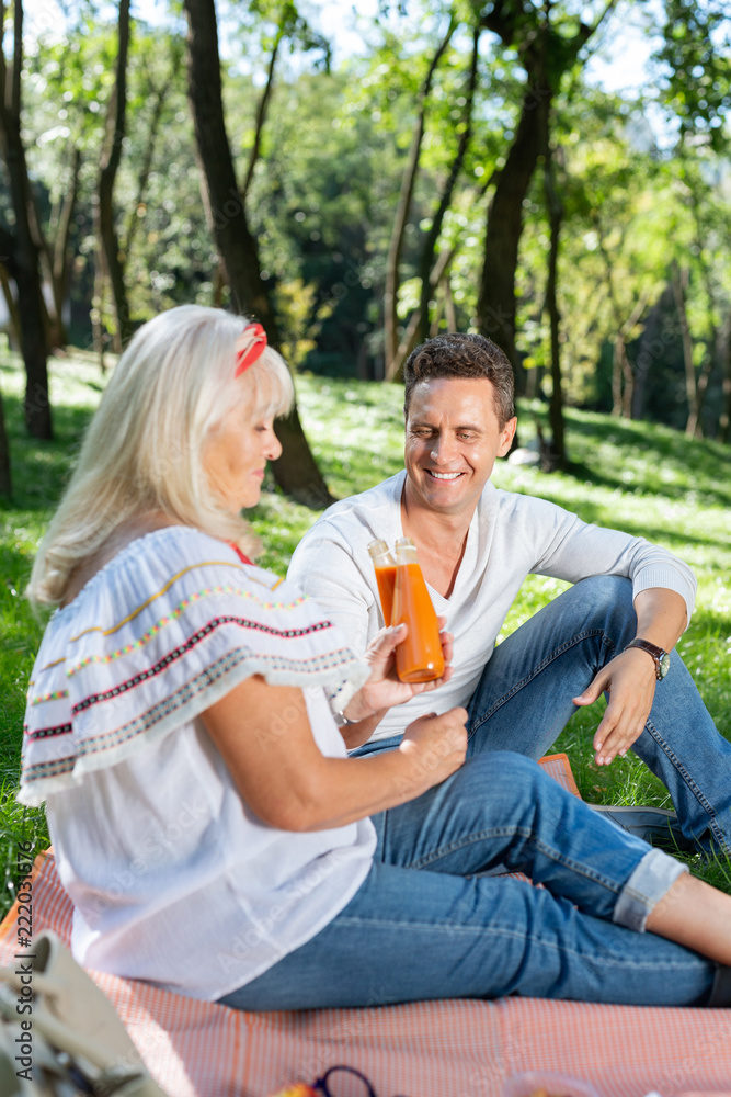 Fresh juice. Pleased young male feeling happiness while communicating with his mature mom Fresh juice. Pleased young male feeling happiness while communicating with his mature mom