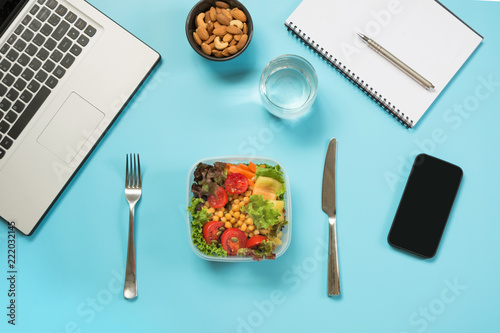 Healthy business lunch in office, salad, almonds, water on blue. Top view with copy space. Concept healthy nutrition. Lunchbox. To do list.