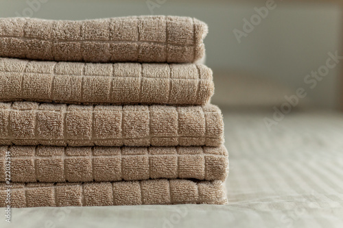 Stack of beige hotel towel on bed in bedroom interior. Soft focus.