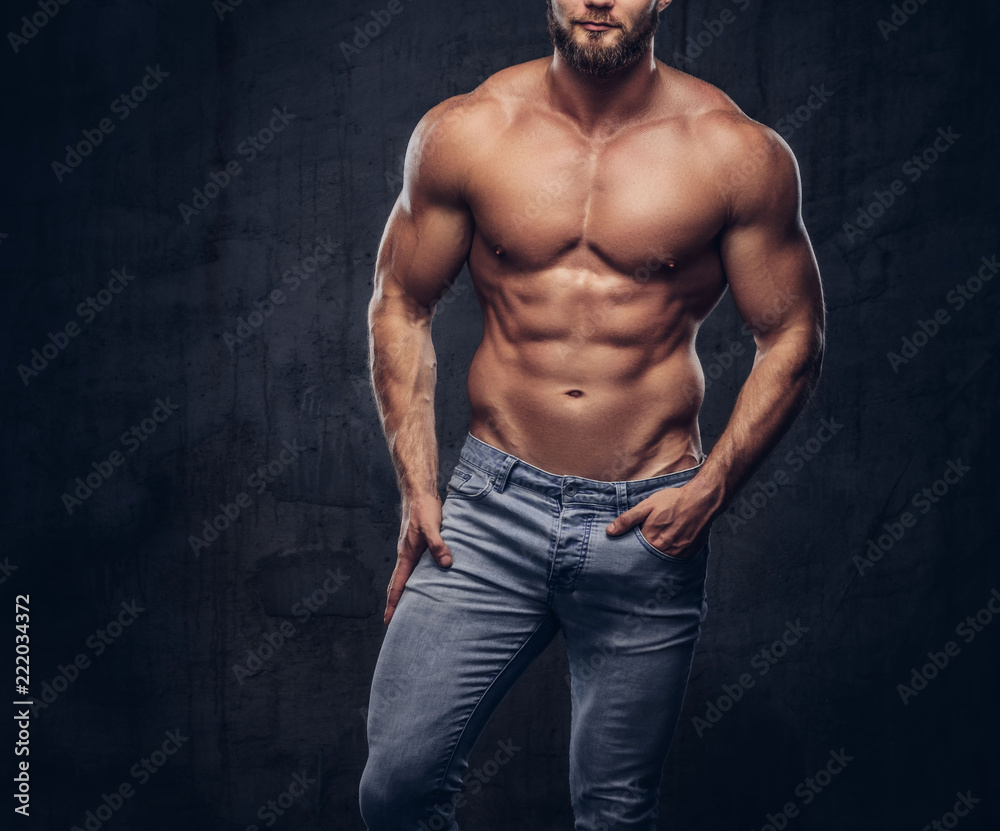 Handsome bearded sporty guy with a muscular body in jeans posing in studio.