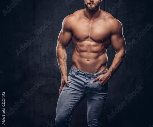 фотография Handsome bearded sporty guy with a muscular body in jeans posing in studio