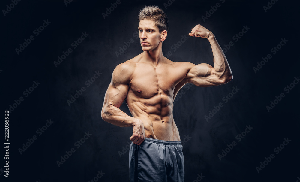 Handsome shirtless man with stylish hair and muscular ectomorph shows his bicep on the dark textured background. Stock Adobe Stock