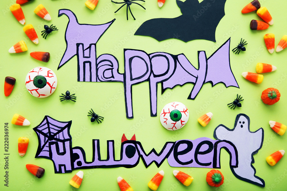 Inscription Happy Halloween with candies and paper decorations on green background Inscription Happy Halloween with candies and paper decorations on green background