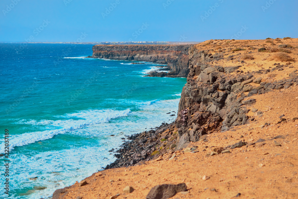 Stunning cliff with rocks and sand overlooking the ocean and blue sky in Fuerteventura, Canary Islands, Spain