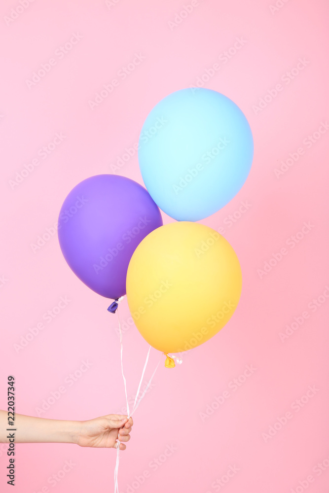 Female hand holding colorful balloons on pink background