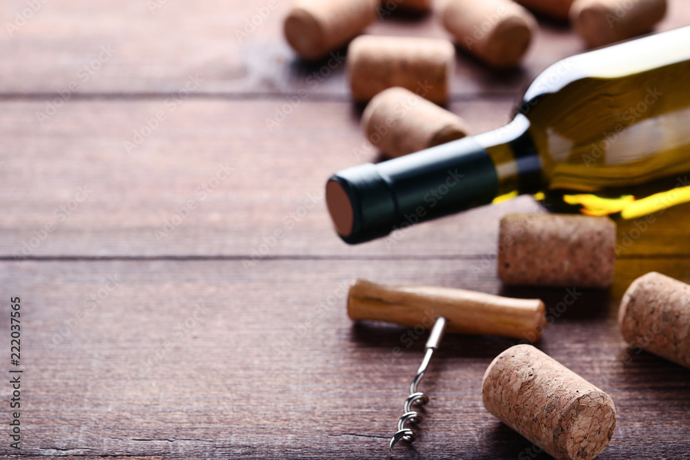 Wine bottle with corks and corkscrew on brown wooden table