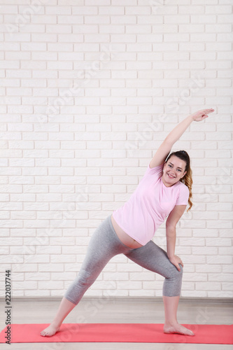 Young pregnant woman doing exercises on brick wall background