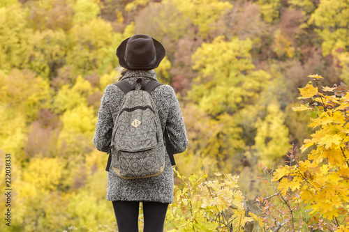 Girl in a hat with a bouquet of yellow leaves. Enjoying of autumn forest. Back view