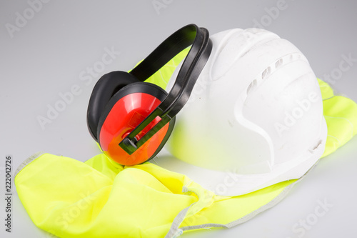 white helmet ear muffs placed on yellow vest with Reflective on white background in safety work concept
