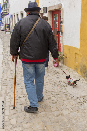 walk of a man in a hat with a small dog on the street of the old town of Obidos