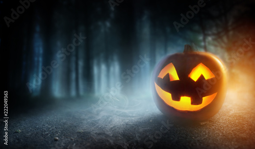 A mysterious and spooky misty halloween evening background with a glowing Jack O Lantern pumpkin.